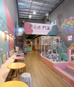 Interior view of a colorful indoor children's playground called "Pixie Play," showing seating, a play structure, and a ball pit.