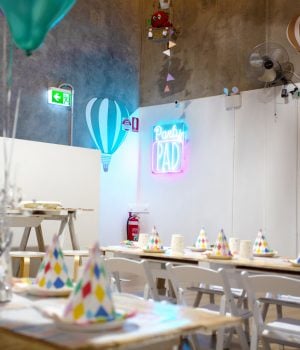An indoor party room decorated with balloons, bunting, and set tables with colorful birthday hats.